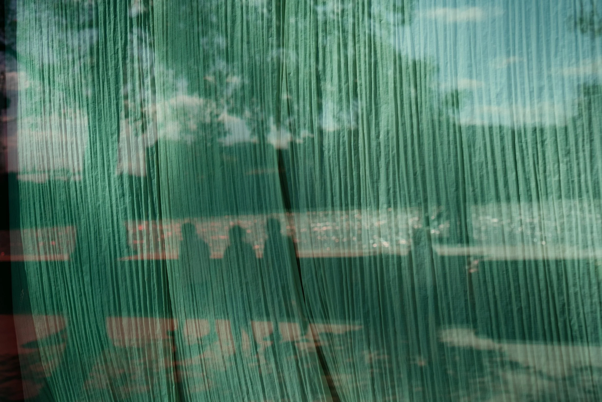 Reflection of trees, sky, and clouds on painted green window blinds.
