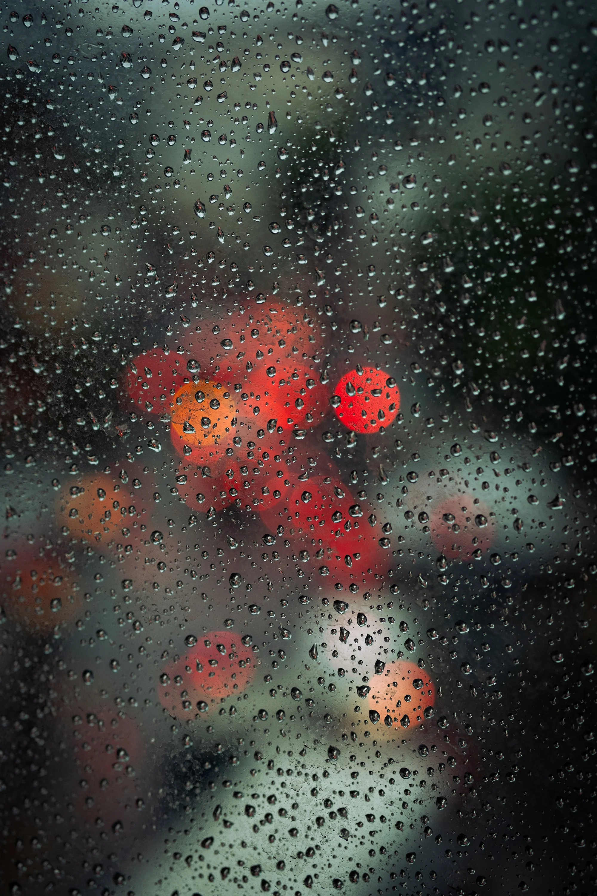 Rain-covered window with blurred red, orange, and yellow traffic lights in the background.