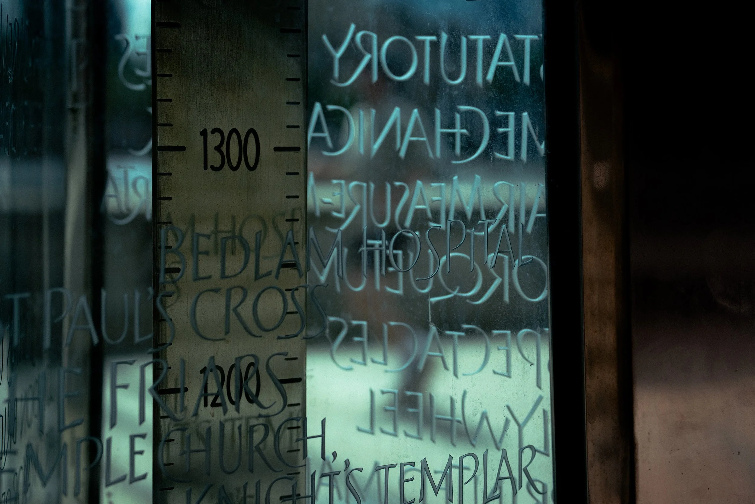 Close-up of a reflective glass surface with carved text, showing inverted and partially obscured words and numbers.