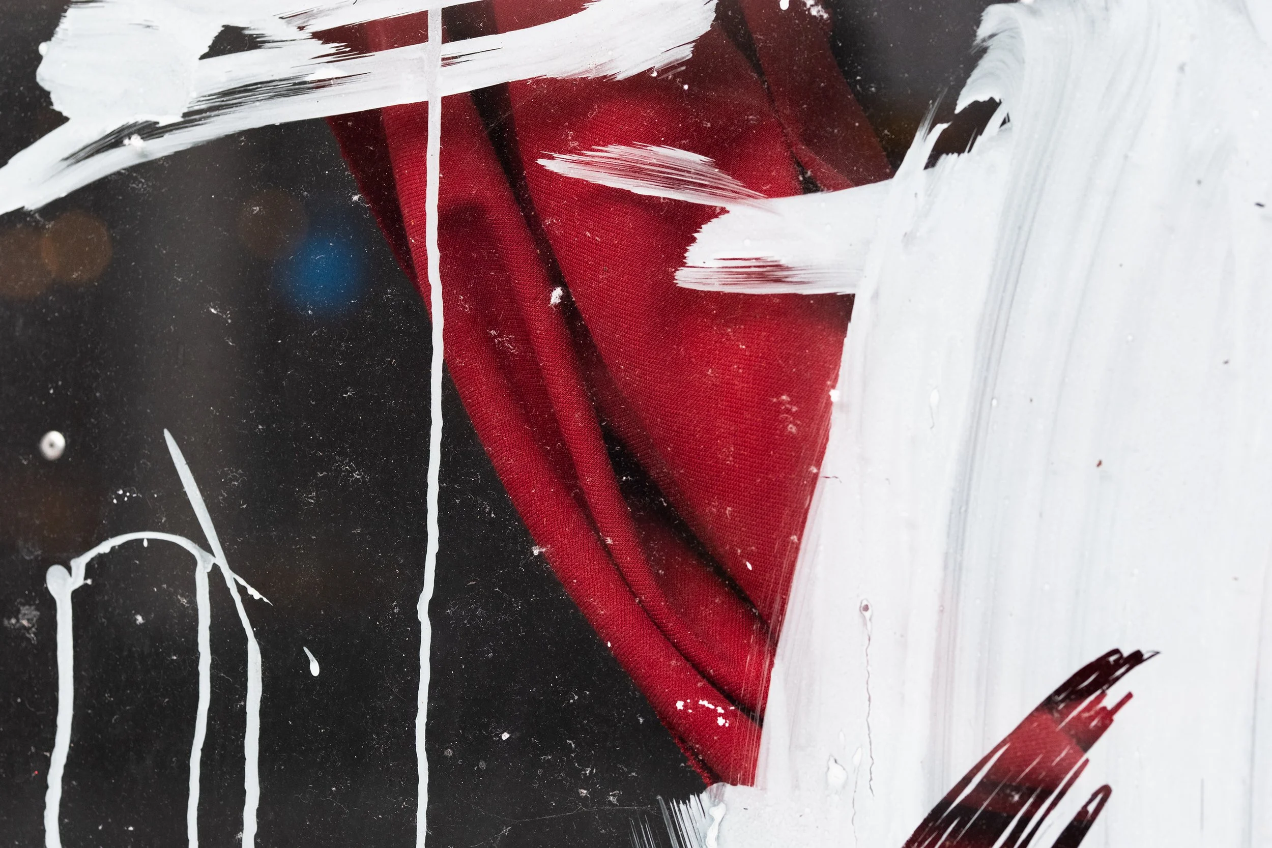 Red fabric partially covered by paint strokes and splatters on a black background.