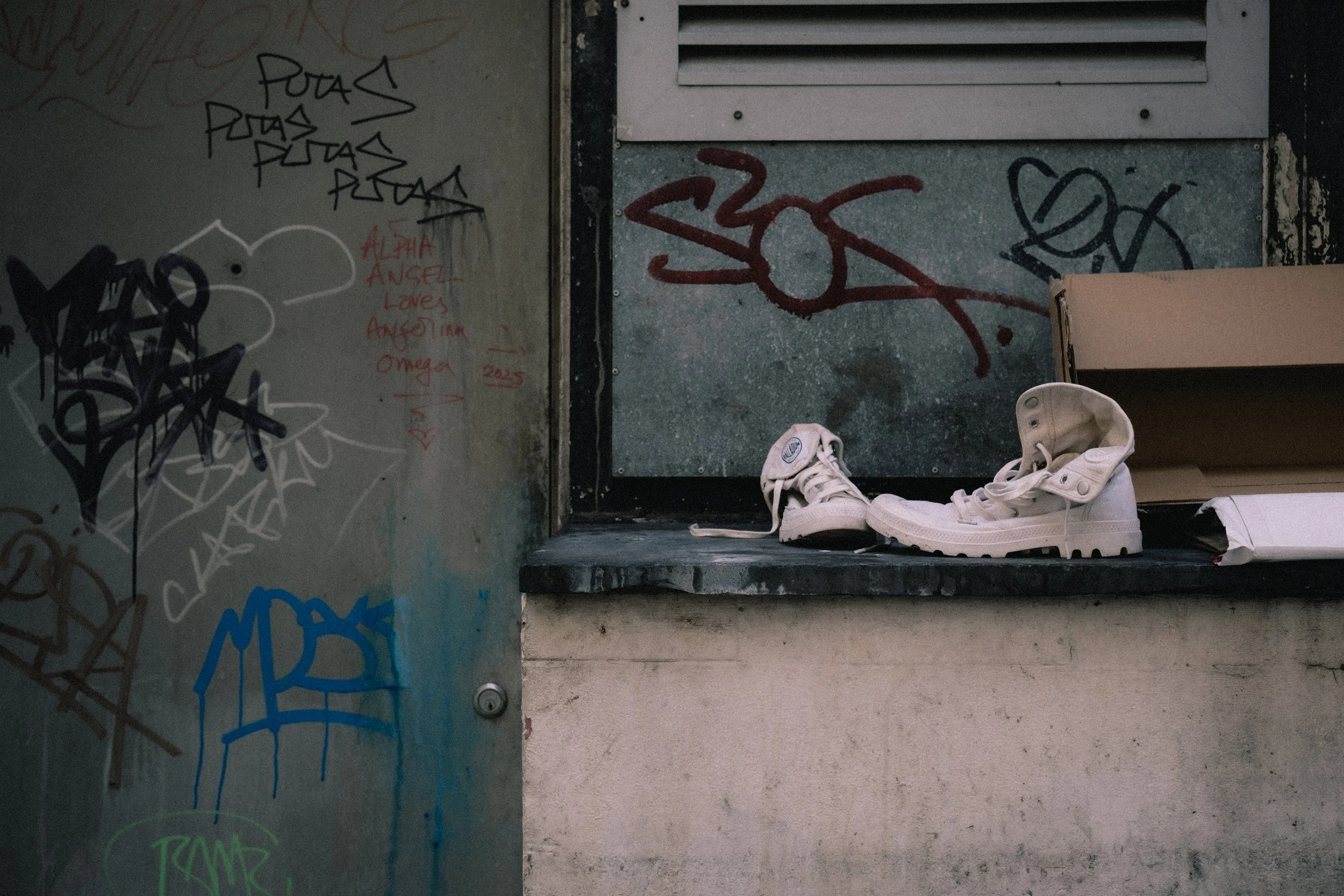 Pair of white sneakers placed on a concrete ledge in an urban setting with graffiti on the walls.