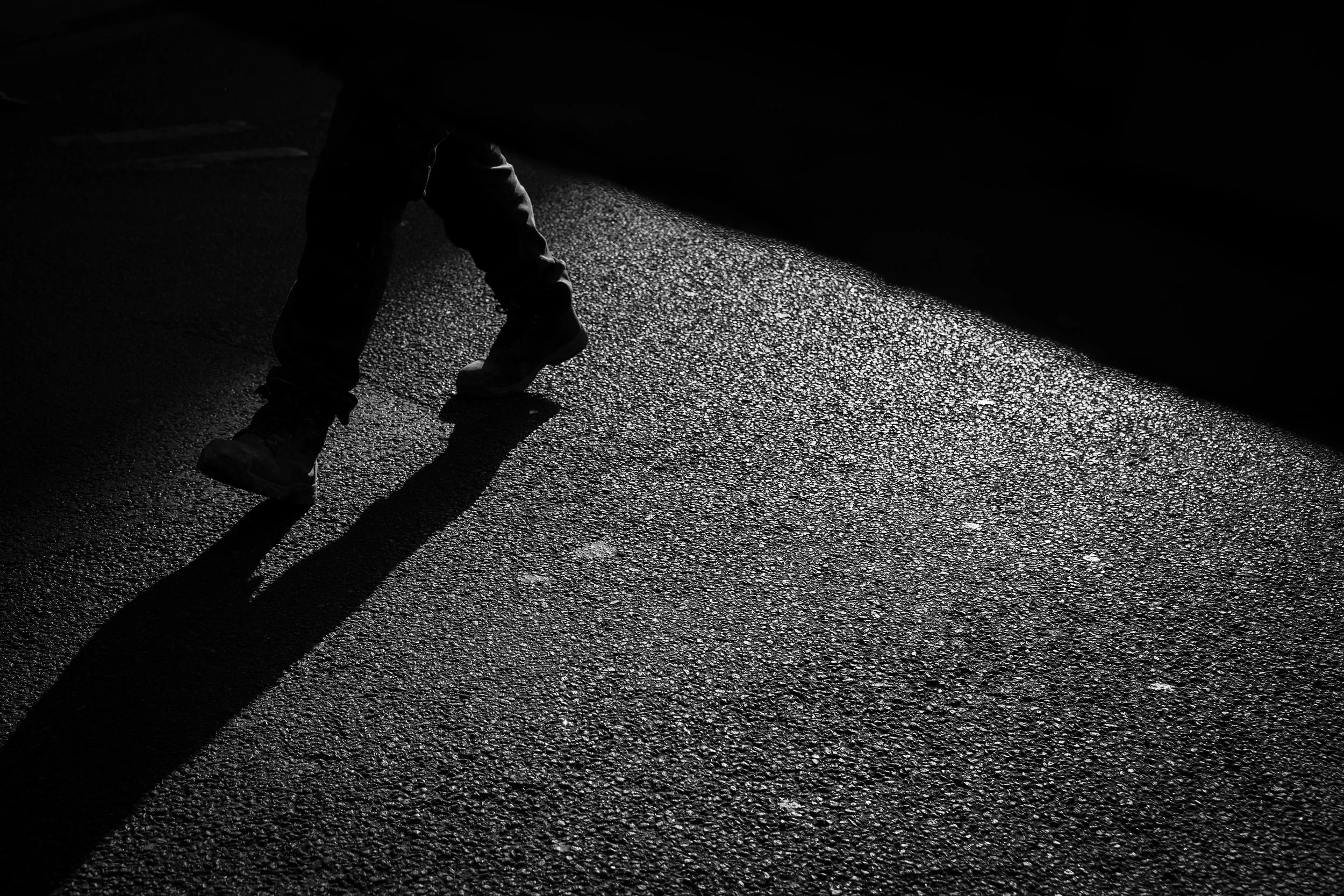 A person walking on a dark pavement, with one foot in the air and the shadow cast on the ground.