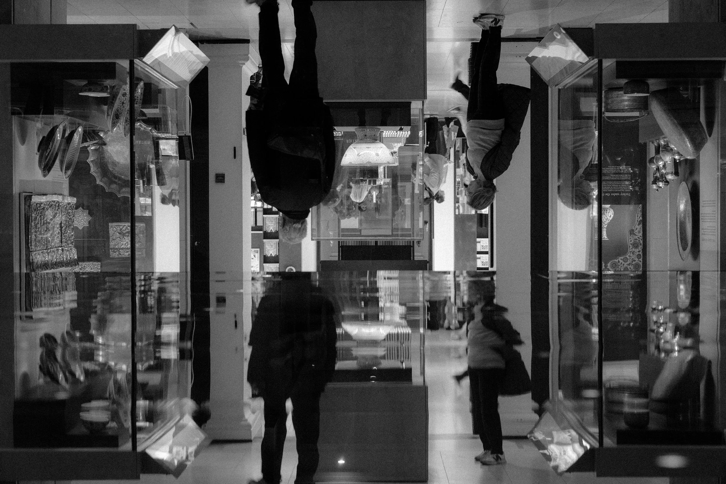 People looking at glass display cases in a museum, with the room being reflected in the displays.