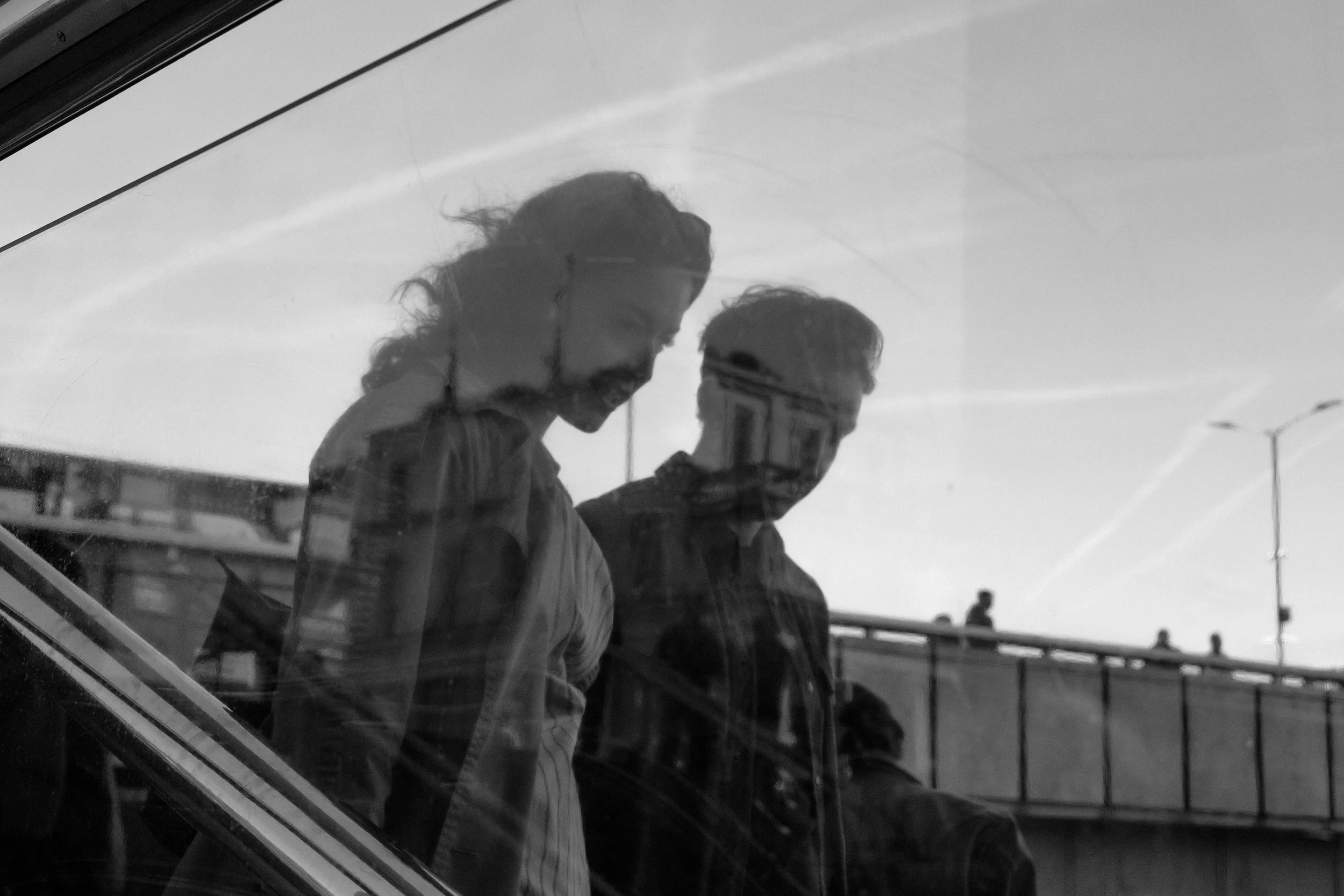 Reflected image of a man and woman walking down stairs, seen through glass , with an urban background.