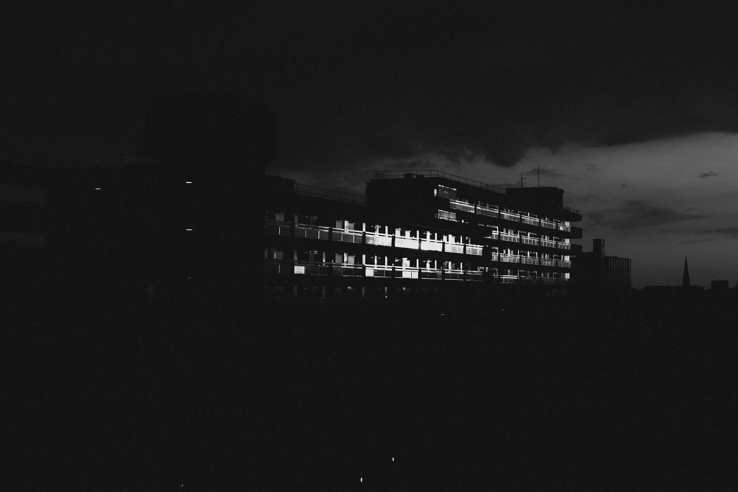 Nighttime cityscape with a modern multi-story building illuminated by lights against dark cloudy sky