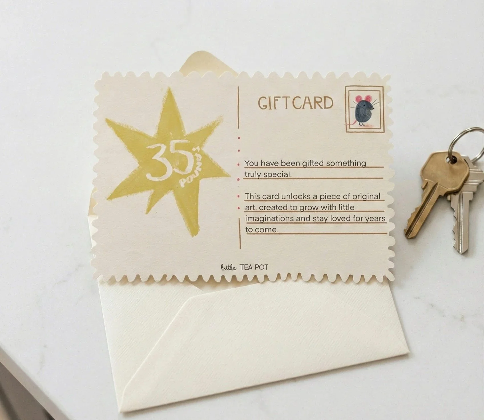 Gift card with yellow star design, text indicating 35% off, and a small mouse illustration in the top right corner. The card is placed on a white envelope with keys nearby.
