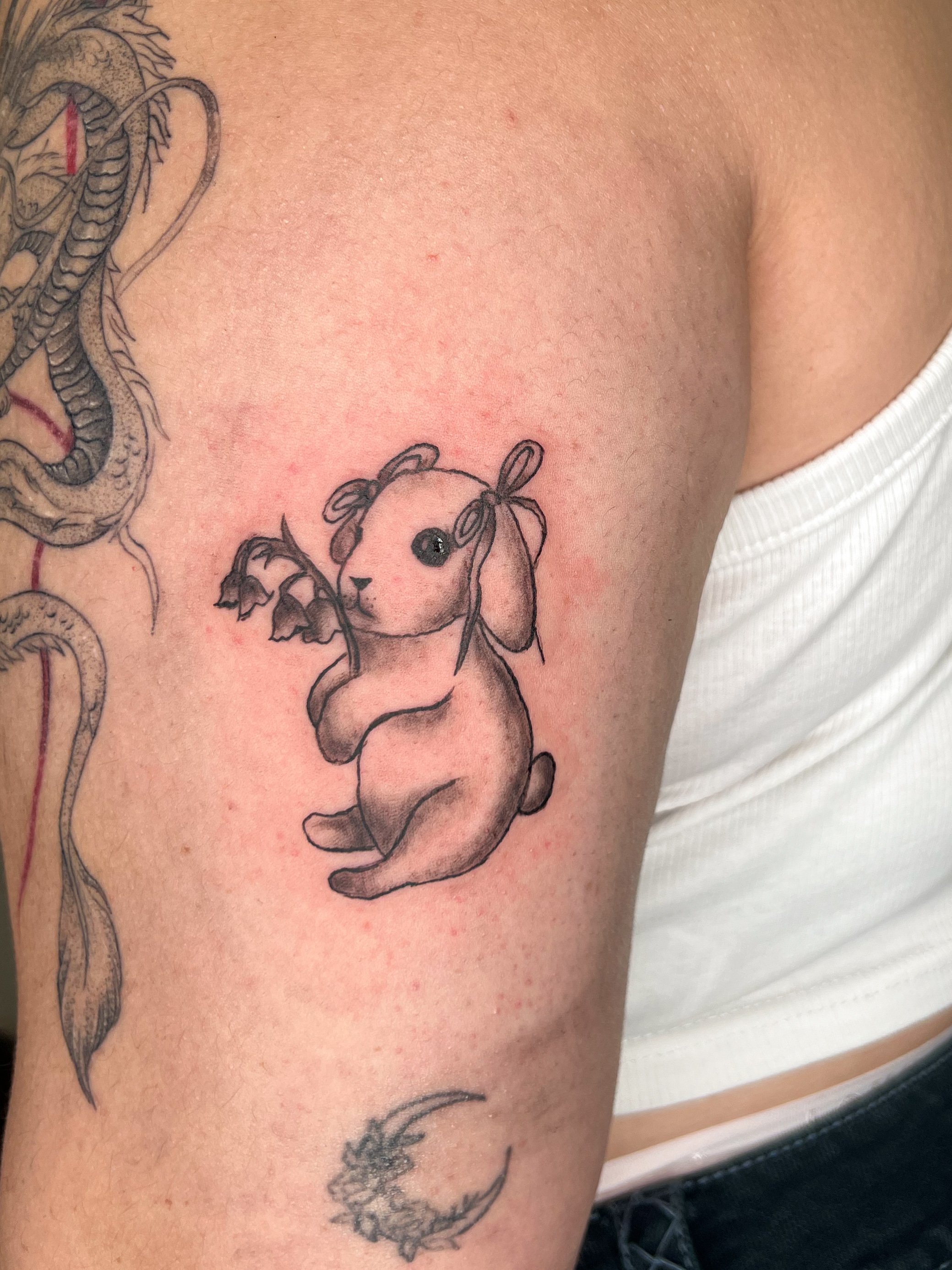 tattoo of a cute bunny holding a small branch with leaves on inner upper arm.