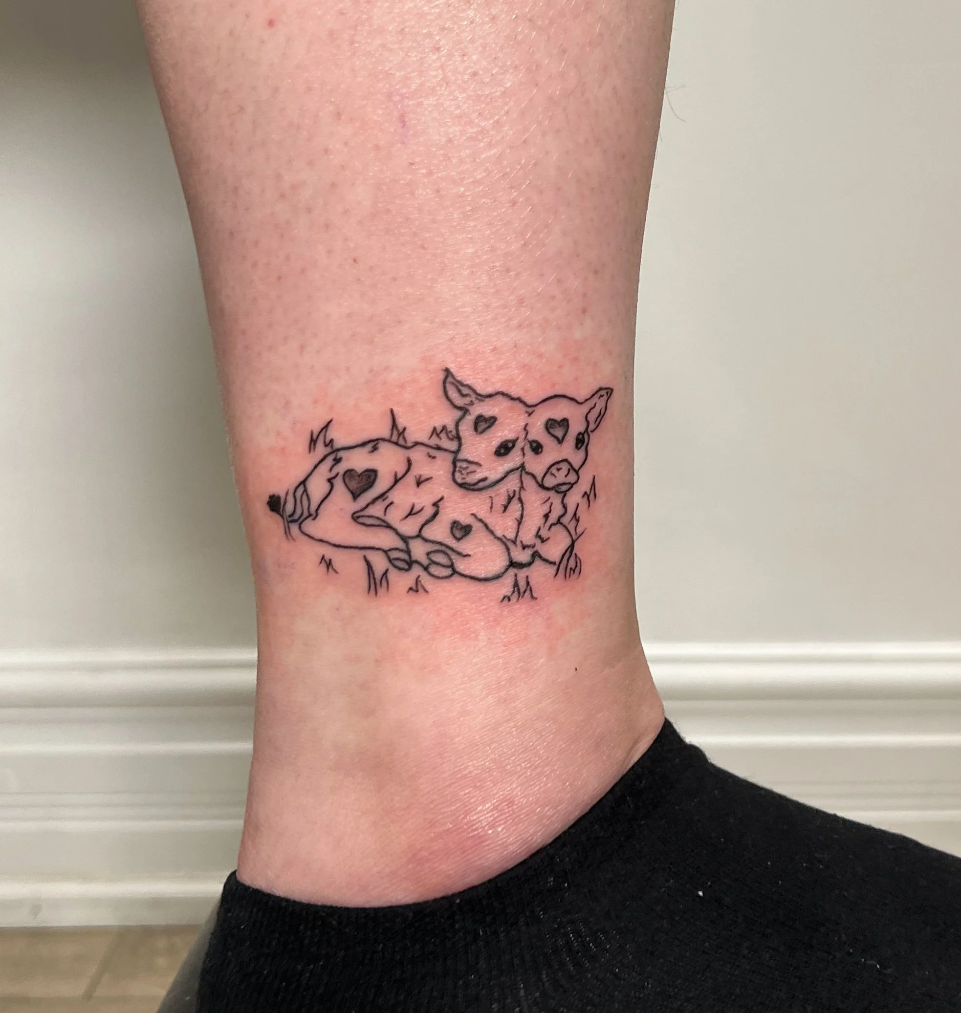 Line art tattoo of a resting puppy with heart-shaped markings on its body and face, positioned on the ankle.