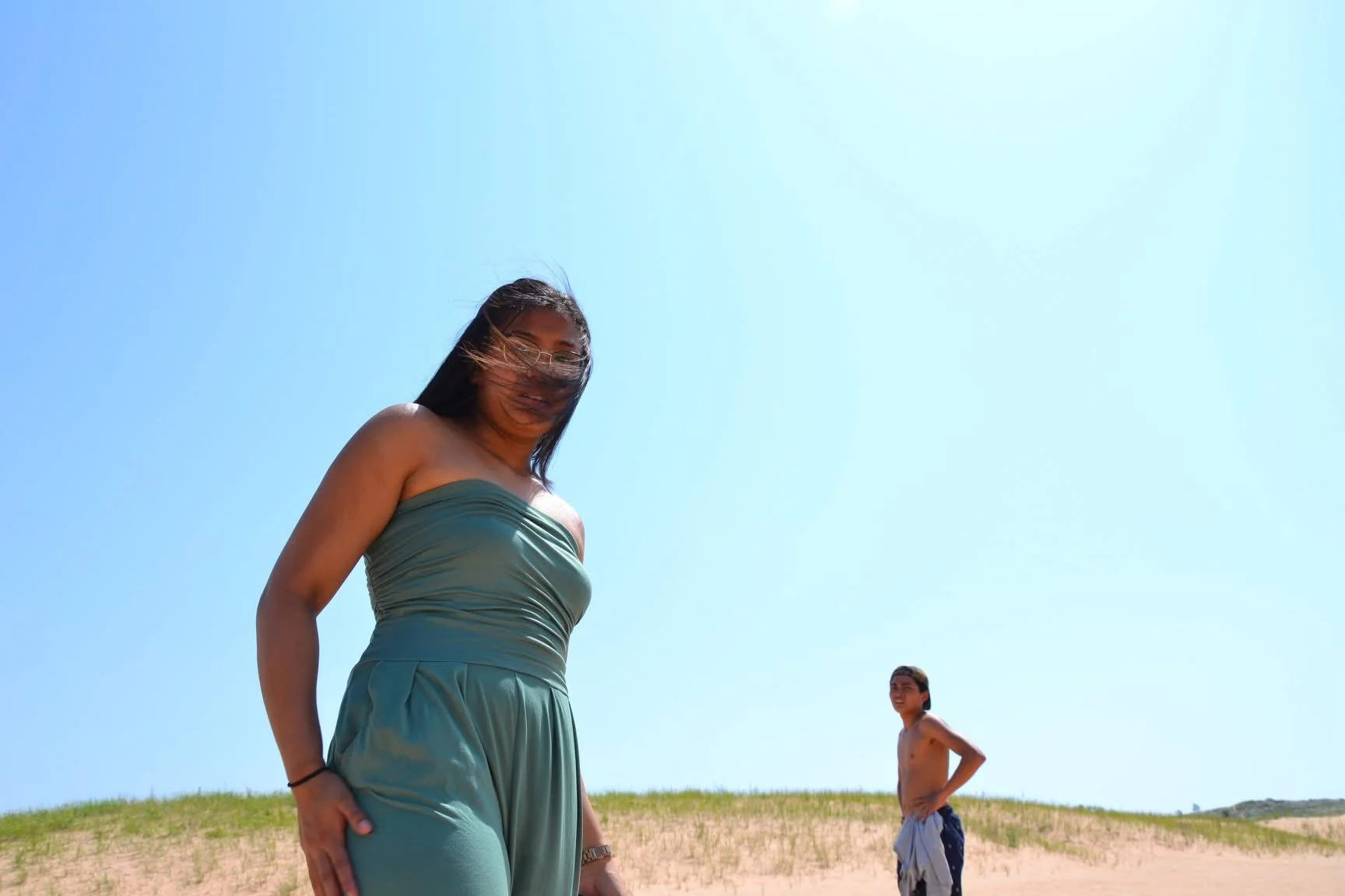 A woman and a boy standing on a sandy hill under a clear blue sky.