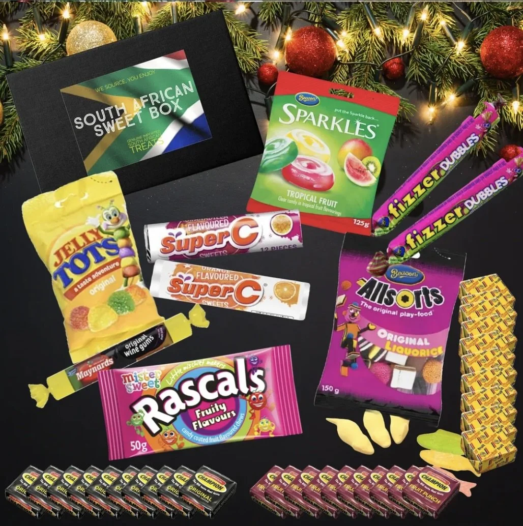 Assorted South African candies and sweets arranged on a black surface with Christmas tree branches and decorations in the background.