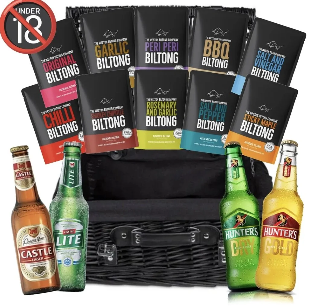 A black picnic basket filled with various flavors of Weston Biltong Company Biltong packages, including Original, Garlic, Peri Peri, BBQ, Salt and Vinegar, Chilli, Smokey Chipotle, Rosemary and Garlic, Salt and Pepper, and Sticky Maple. Several bottles of Castle and Hunter’s beer are placed around the basket.