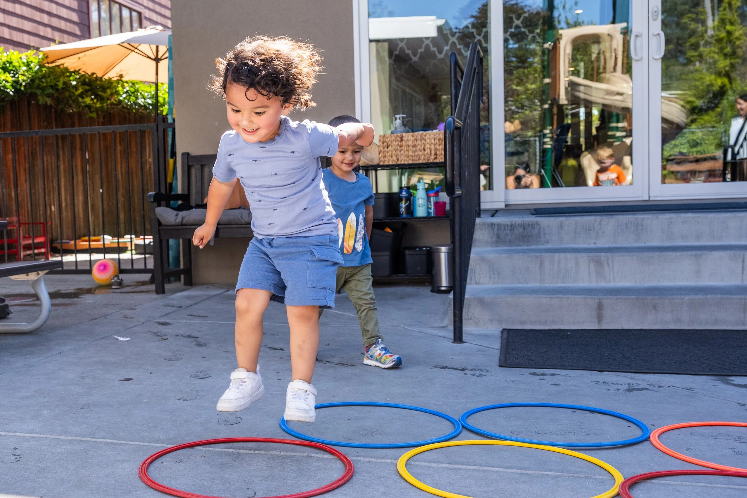 Two children playing a game with colorful hoops on a concrete patio outside a house.