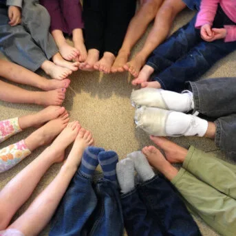 Children and adults sitting in a circle on the floor, holding hands to form a heart shape.