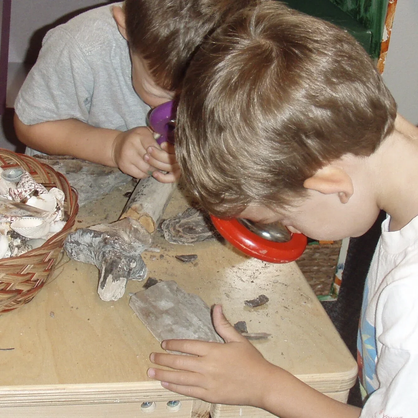 Two children examining rocks and fossils on a table, using magnifying glasses.