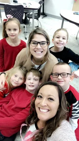 Group of six children and two adults smiling in a classroom.