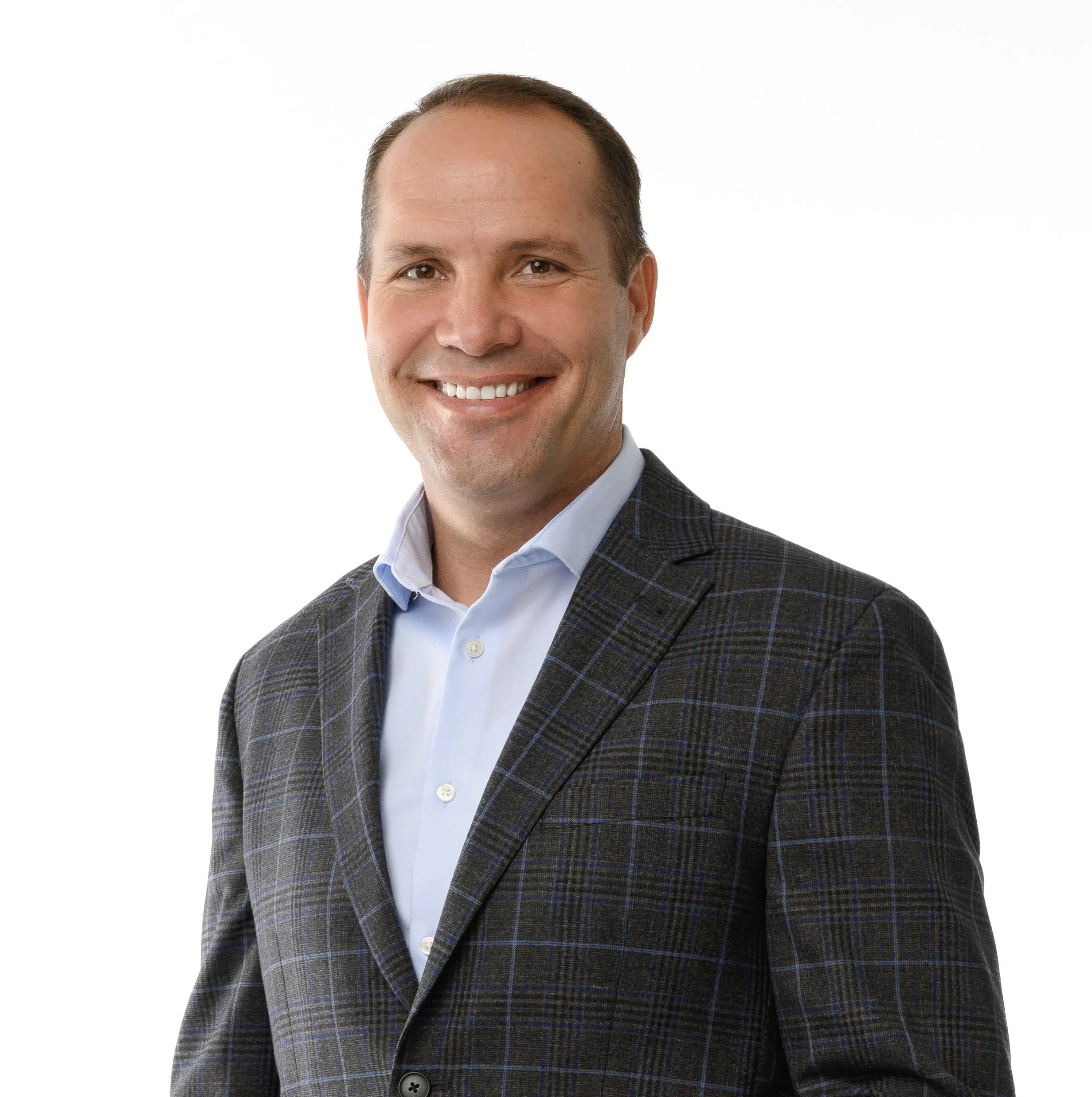 A smiling man in a gray plaid suit and light blue shirt posing against a white background.