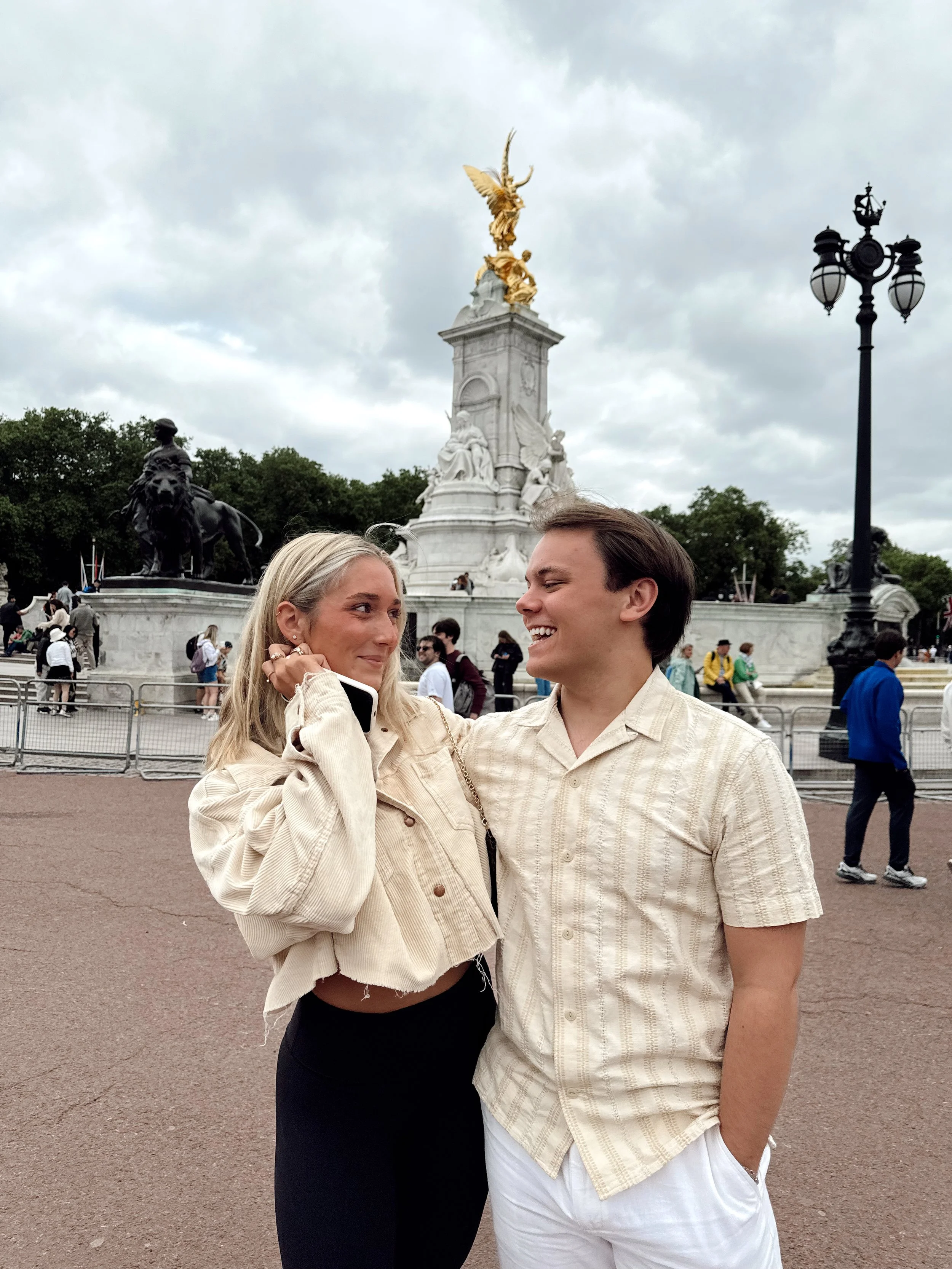 Young woman and man smiling at each other in front of the Victoria Memorial in London, England.