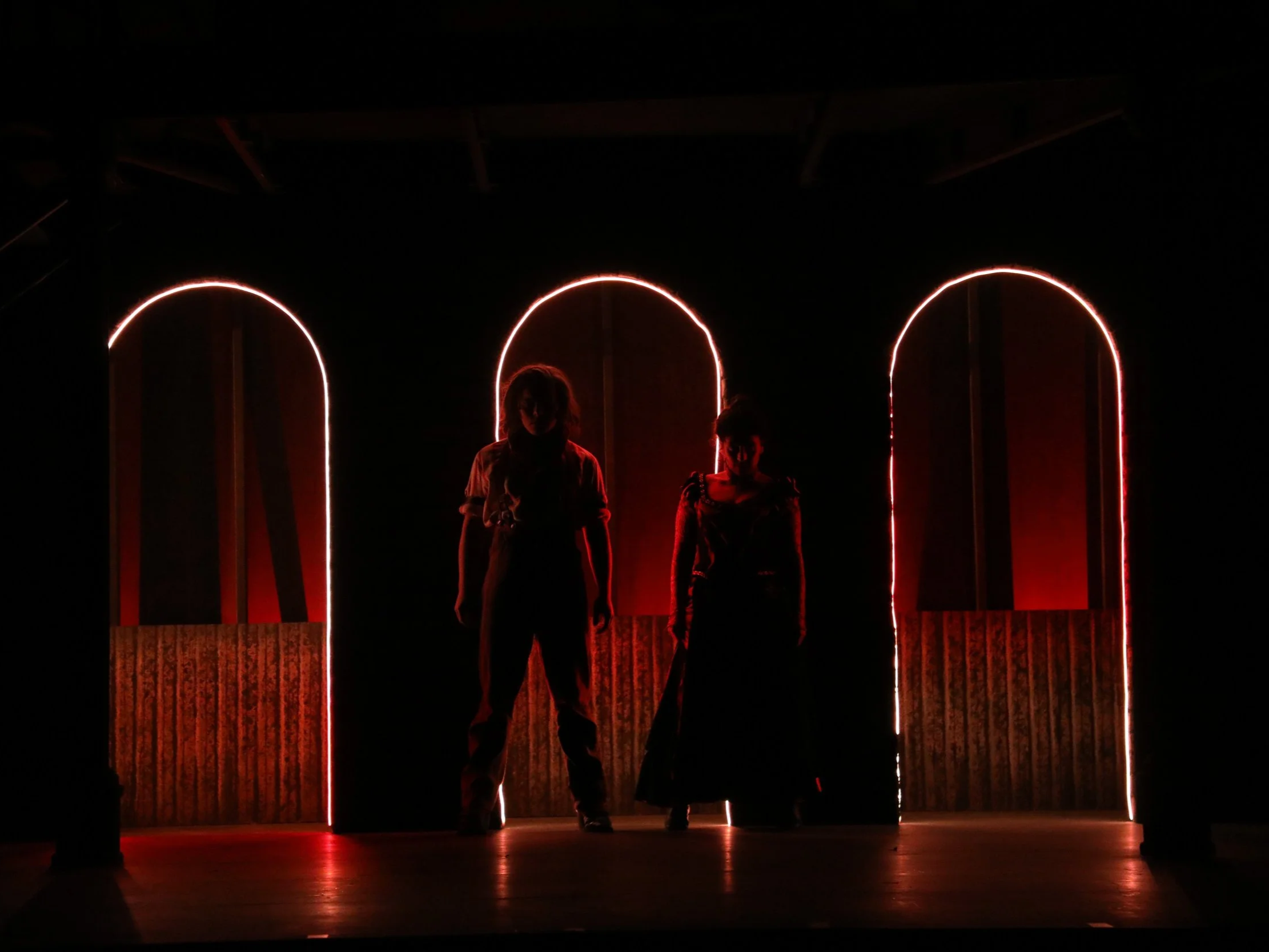 Silhouettes of Sweeney Todd and Mrs. Lovett standing in front of illuminated archways on a dark stage.