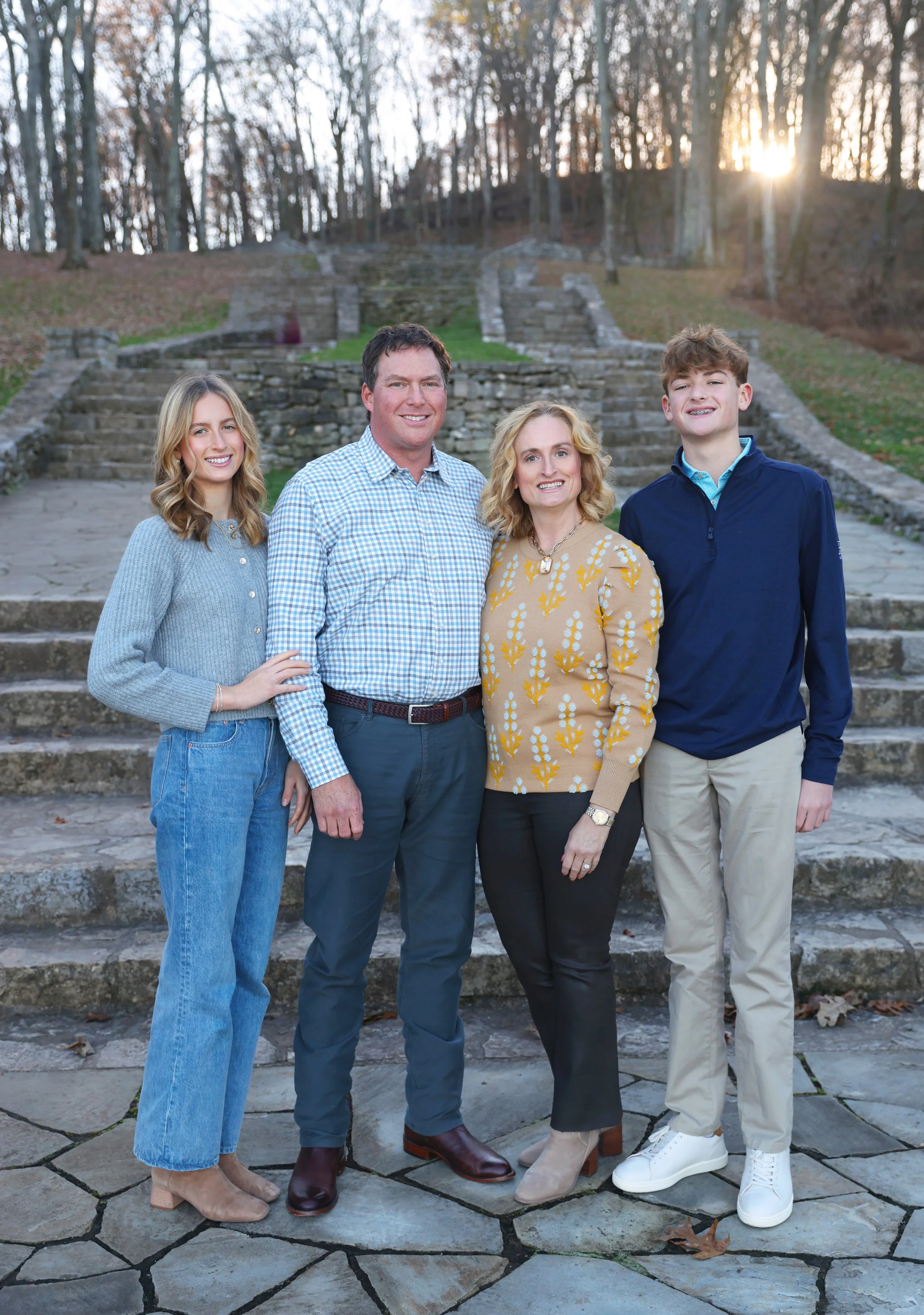 A family of five standing outdoors on stone steps in a park during sunset, smiling at the camera.