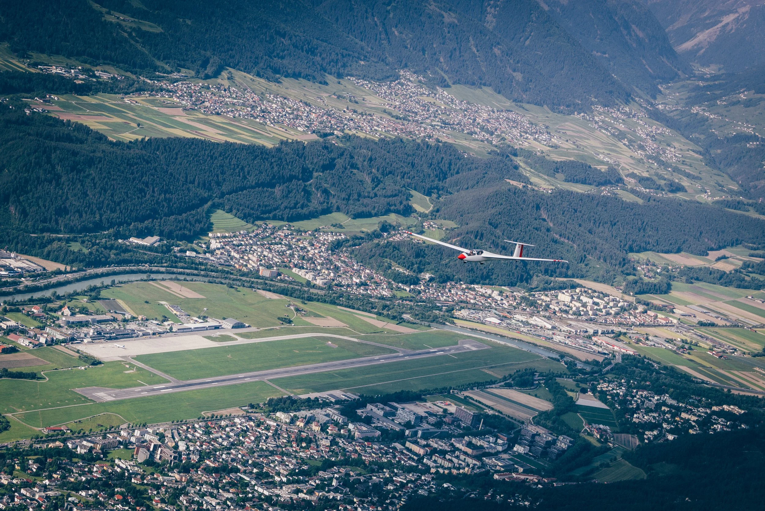 Schweben über einer grünen Landschaft mit Städten, Wäldern, Flüssen und einem startenden Flugzeug in der Luft.