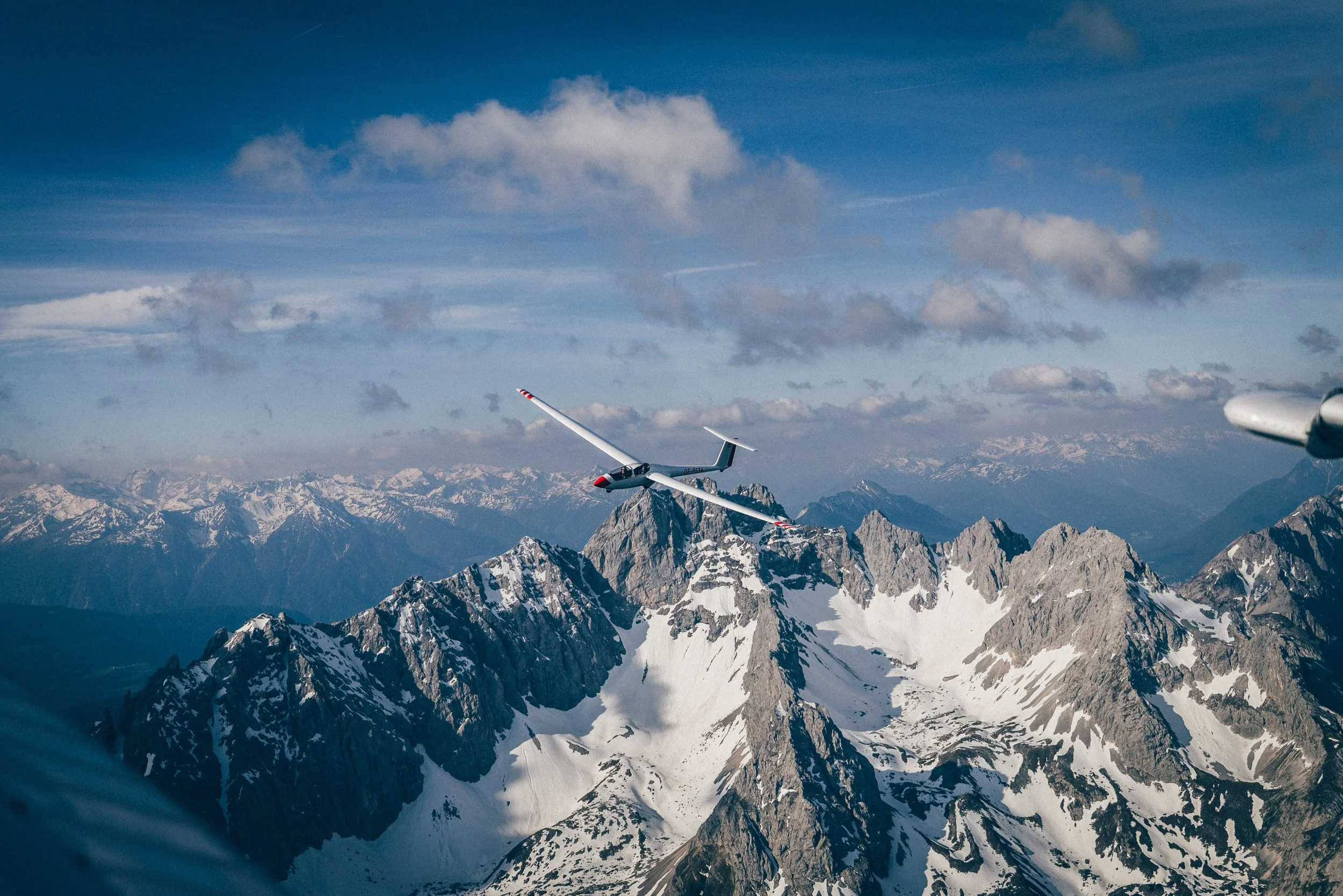 Segelflugzeug fliegt über schneebedeckte Berge in den Alpen bei schönem Himmel.