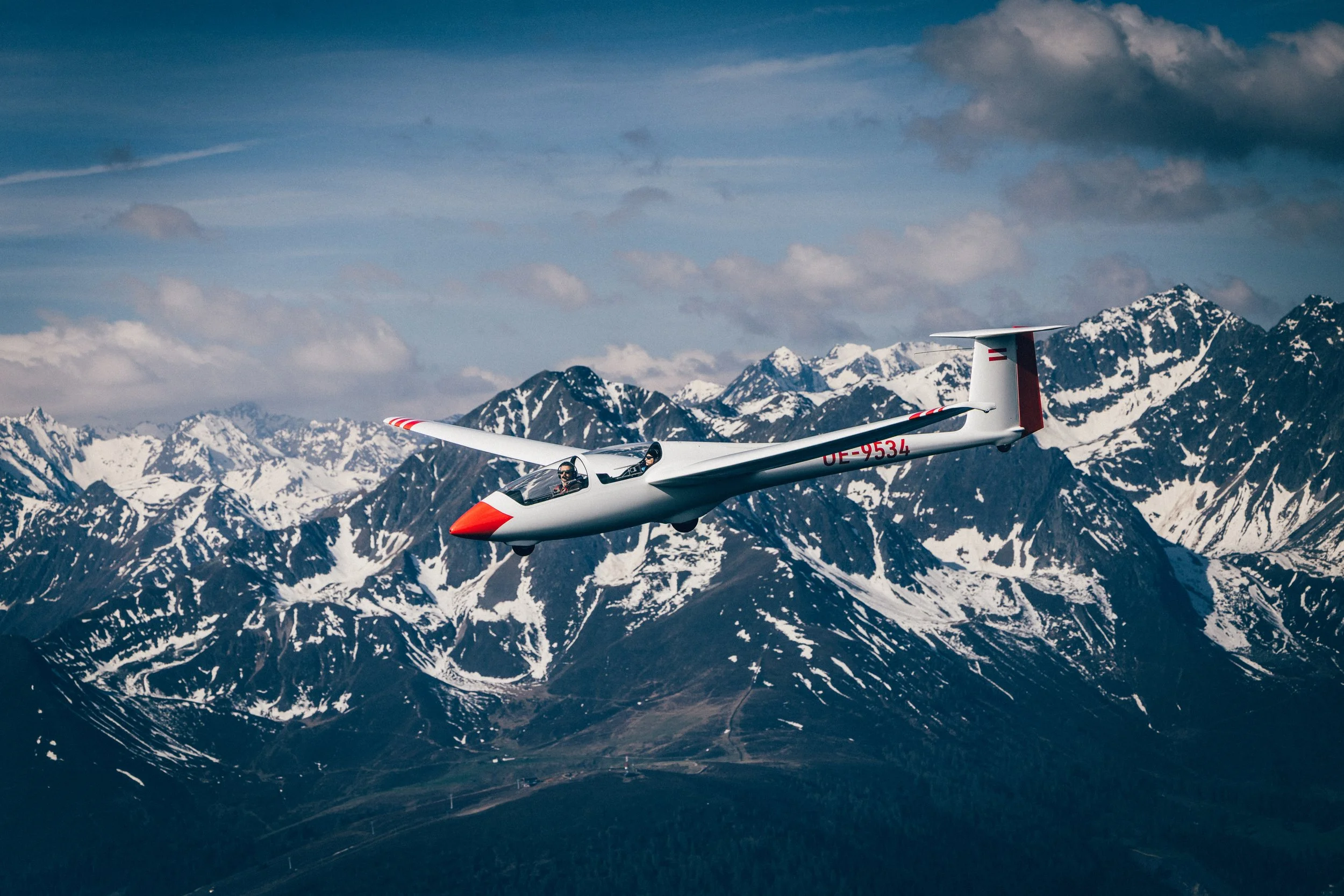 Segelflugzeug fliegt vor einer Bergkulisse mit schneebedeckten Gipfeln.