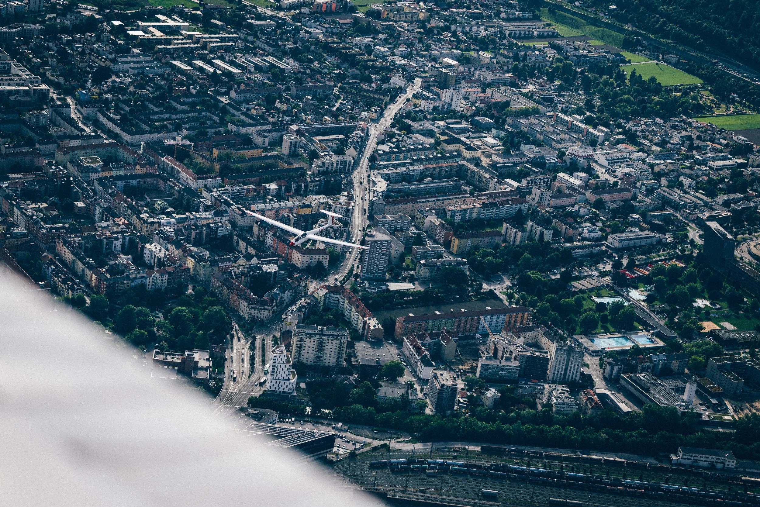 Luftaufnahme einer Stadt mit Gebäuden, Straßen, Grünflächen und einem Windrad.