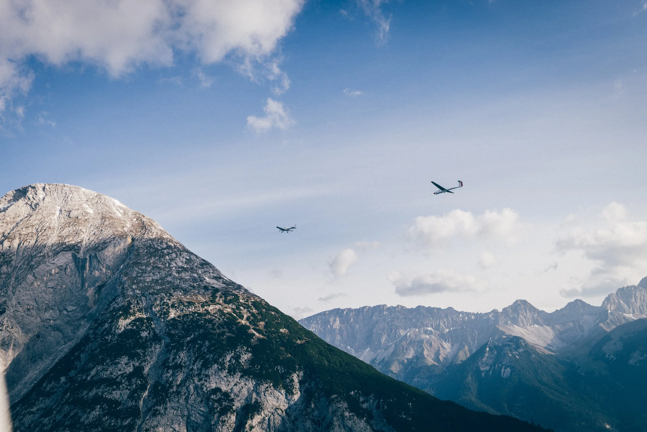 Drei Flugzeuge fliegen über eine schneebedeckte Bergkette am Himmel mit wenigen Wolken.