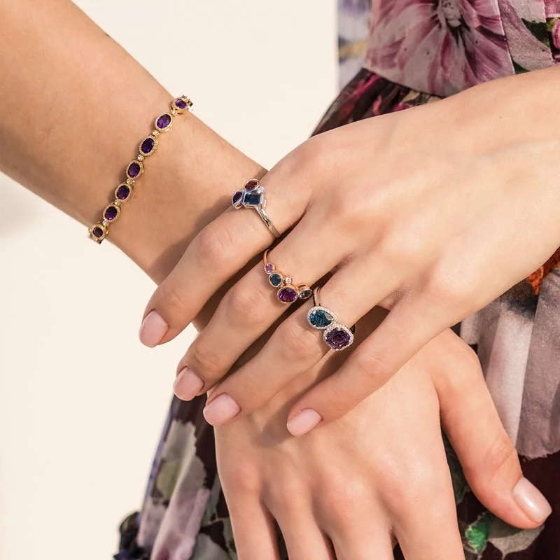 Two hands showing off rings and a bracelet with Amethyst and Sapphire gemstones.