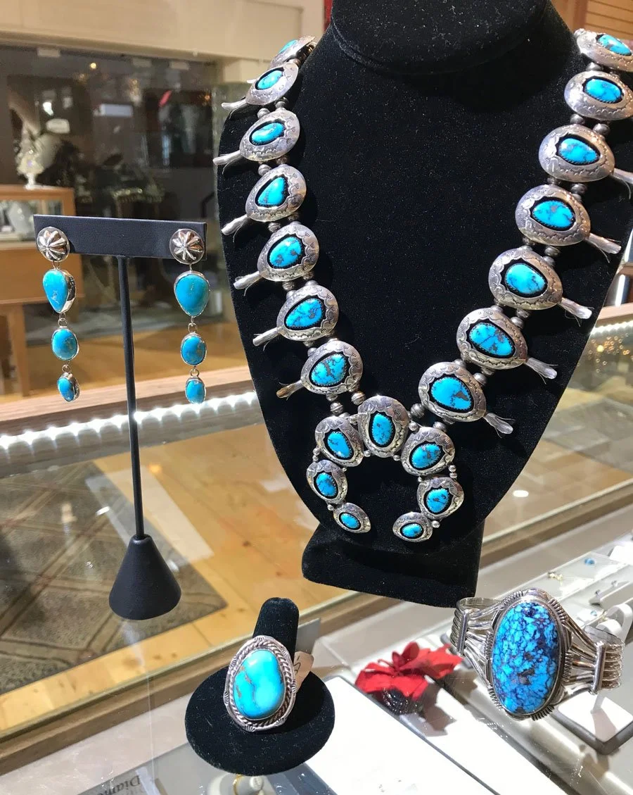 Jewelry display featuring a large turquoise and silver necklace, matching earrings, and a ring, all with turquoise stones, in a jewelry store.
