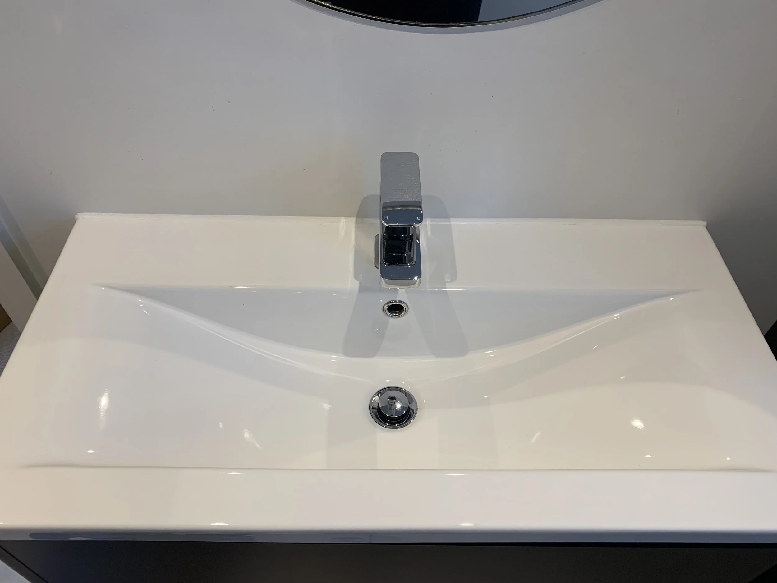 White bathroom sink with a modern chrome faucet and a wall behind it.