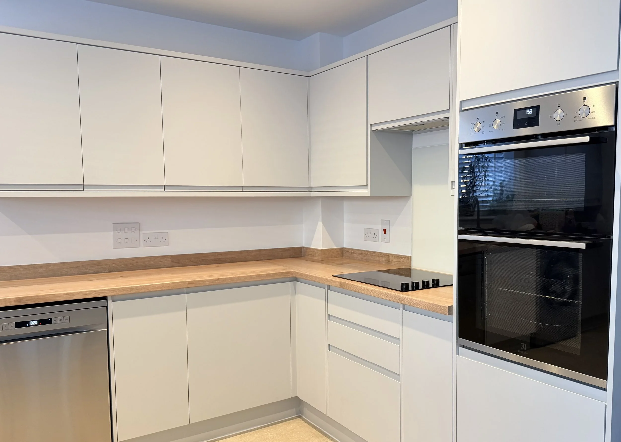 Modern kitchen with white cabinets, wooden countertop, black stovetop, stainless steel oven, and dishwasher after our standard cleaning services.