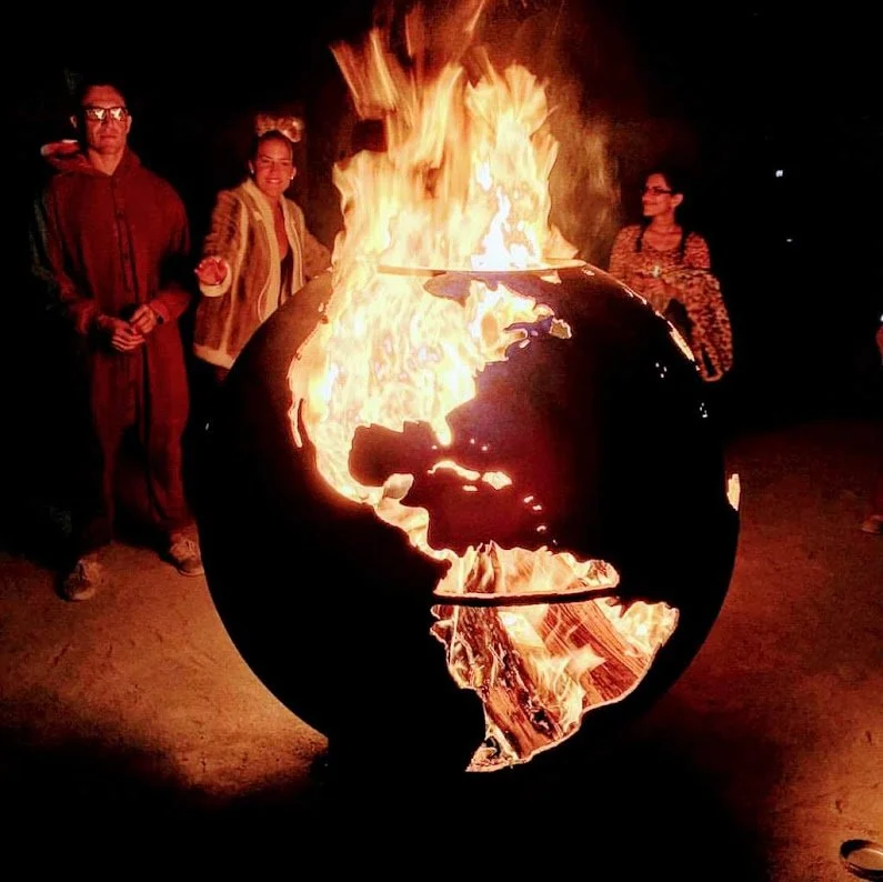 Group of people standing around a fiery globe sculpture at night.