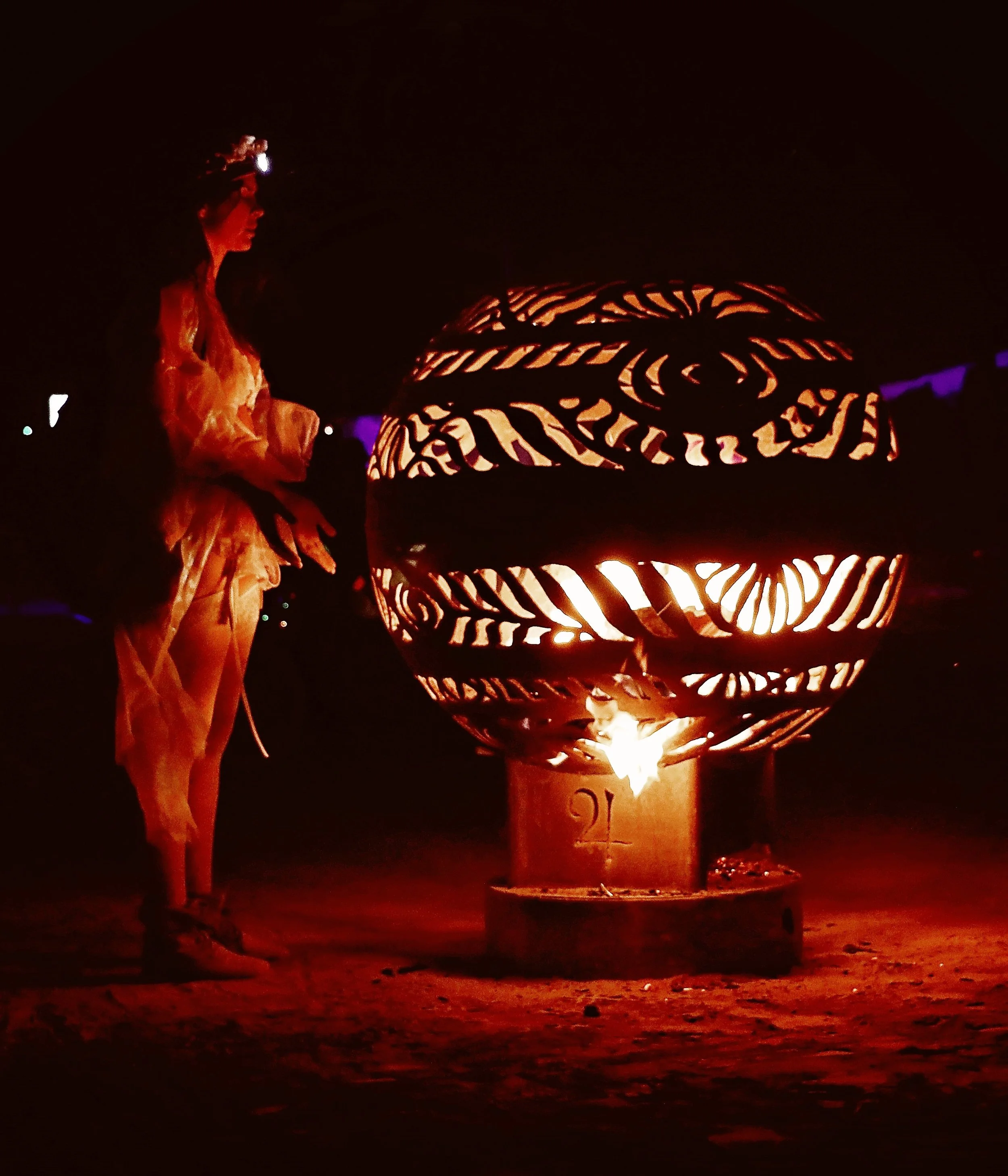 Person standing next to large decorative fire sculpture glowing with orange light at night.