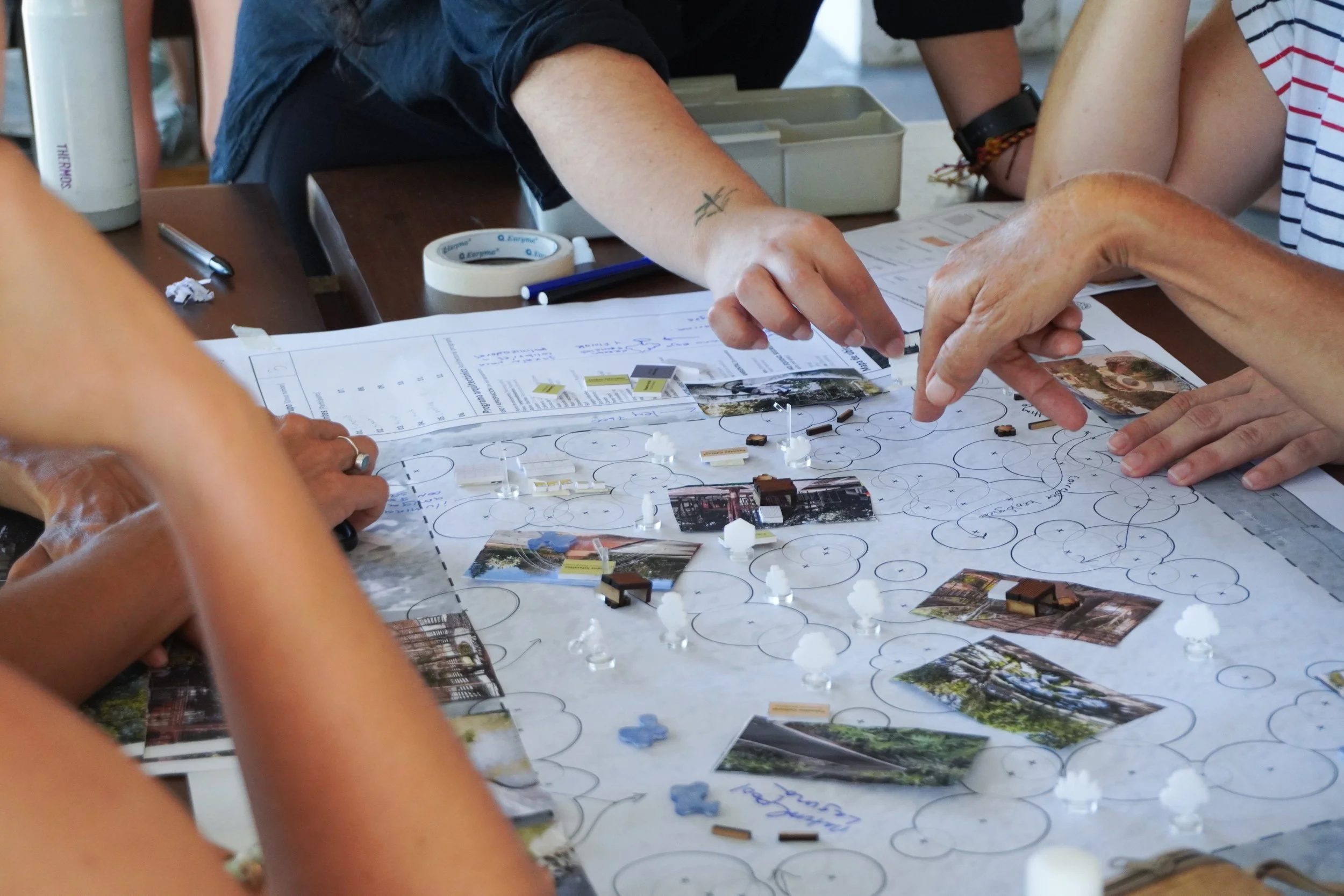 People gathered around a table playing a tabletop game with maps, cards, and small game pieces.