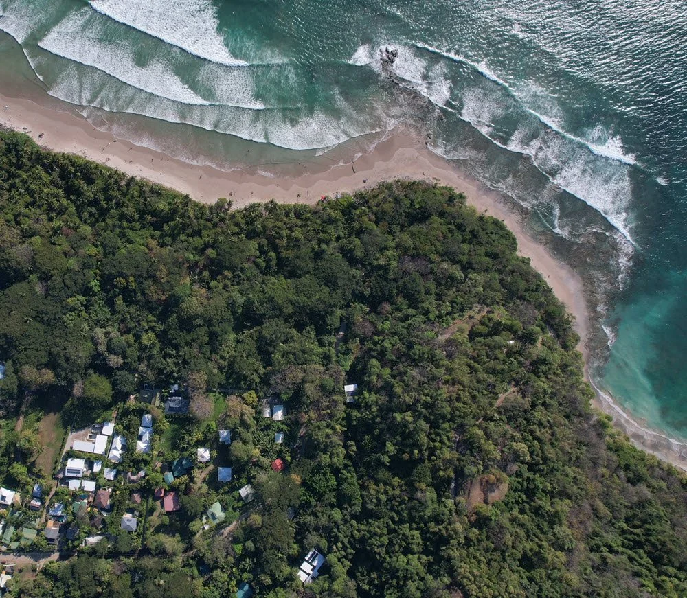 Hermosa, Pueblo San Martín, Cobano, Costa Rica. Aerial view of a lush green forest meeting a sandy beach town with ocean waves.