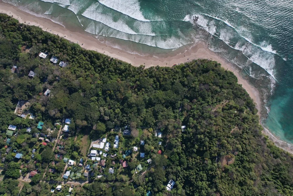 Hermosa, Pueblo San Martín, Cobano, Costa Rica. Aerial view of a lush green forest meeting a sandy beach town with ocean waves.
