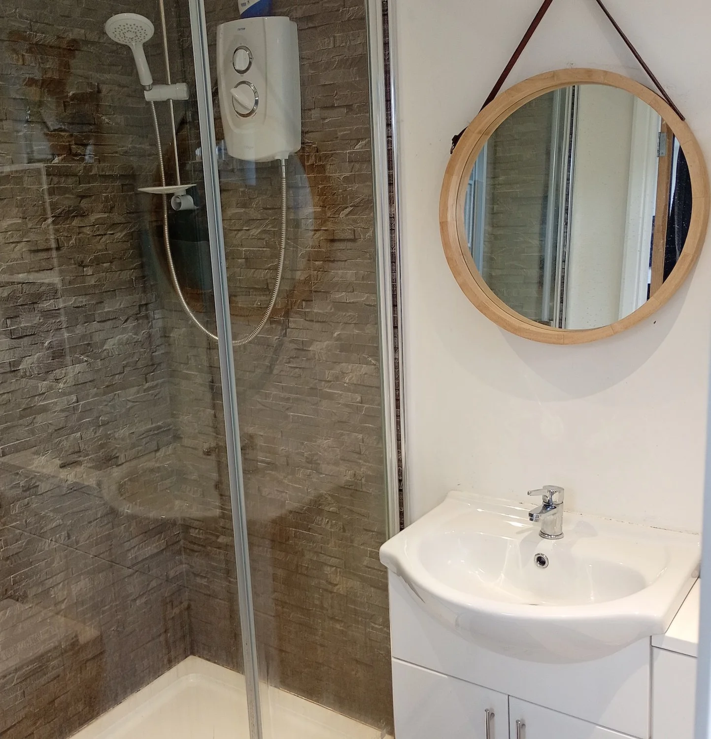 Bathroom with a glass shower enclosure, a small white sink with a mirror above, and a brown textured wall behind the shower.