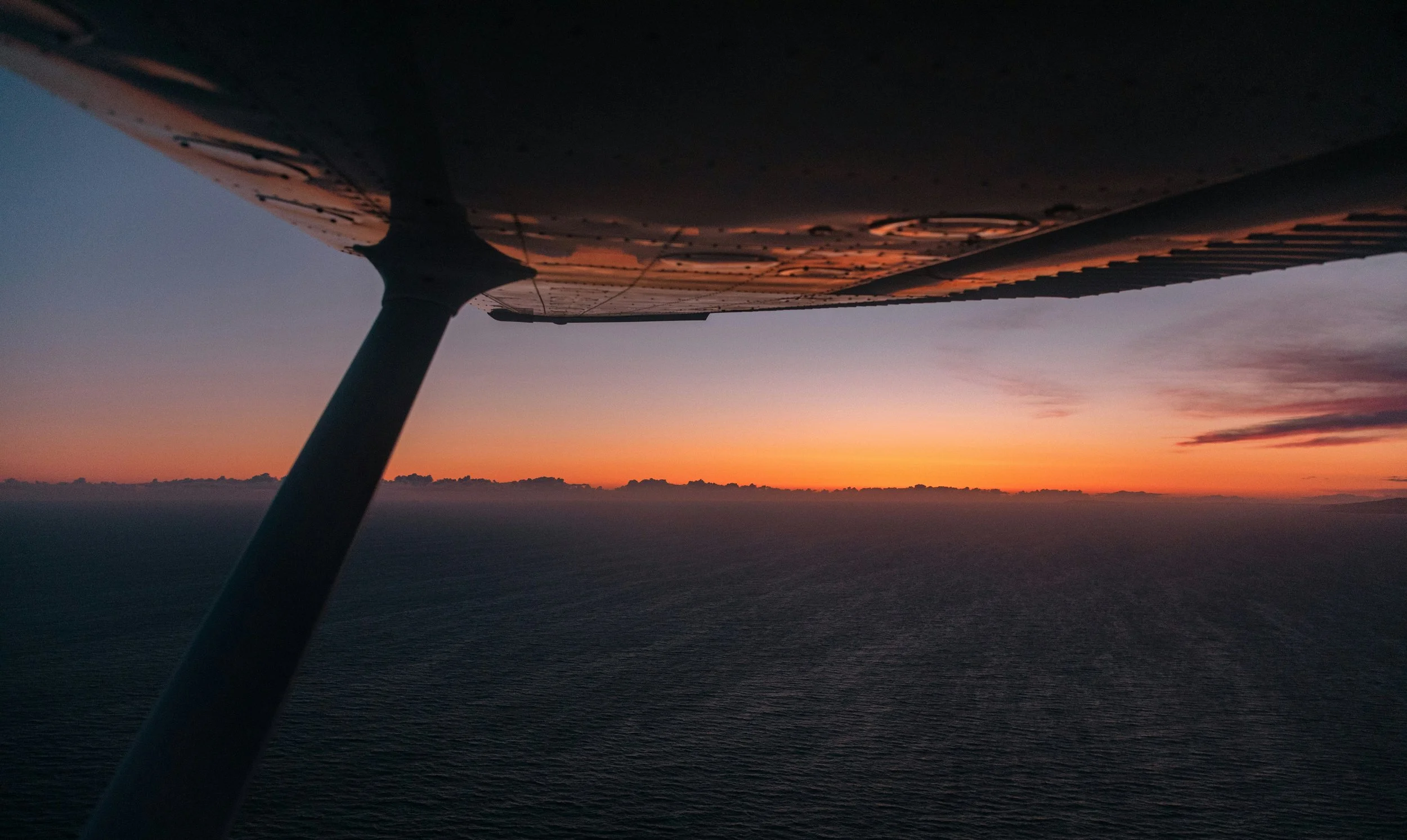 Aerial view from an airplane showing the wing and a sunset over the ocean.