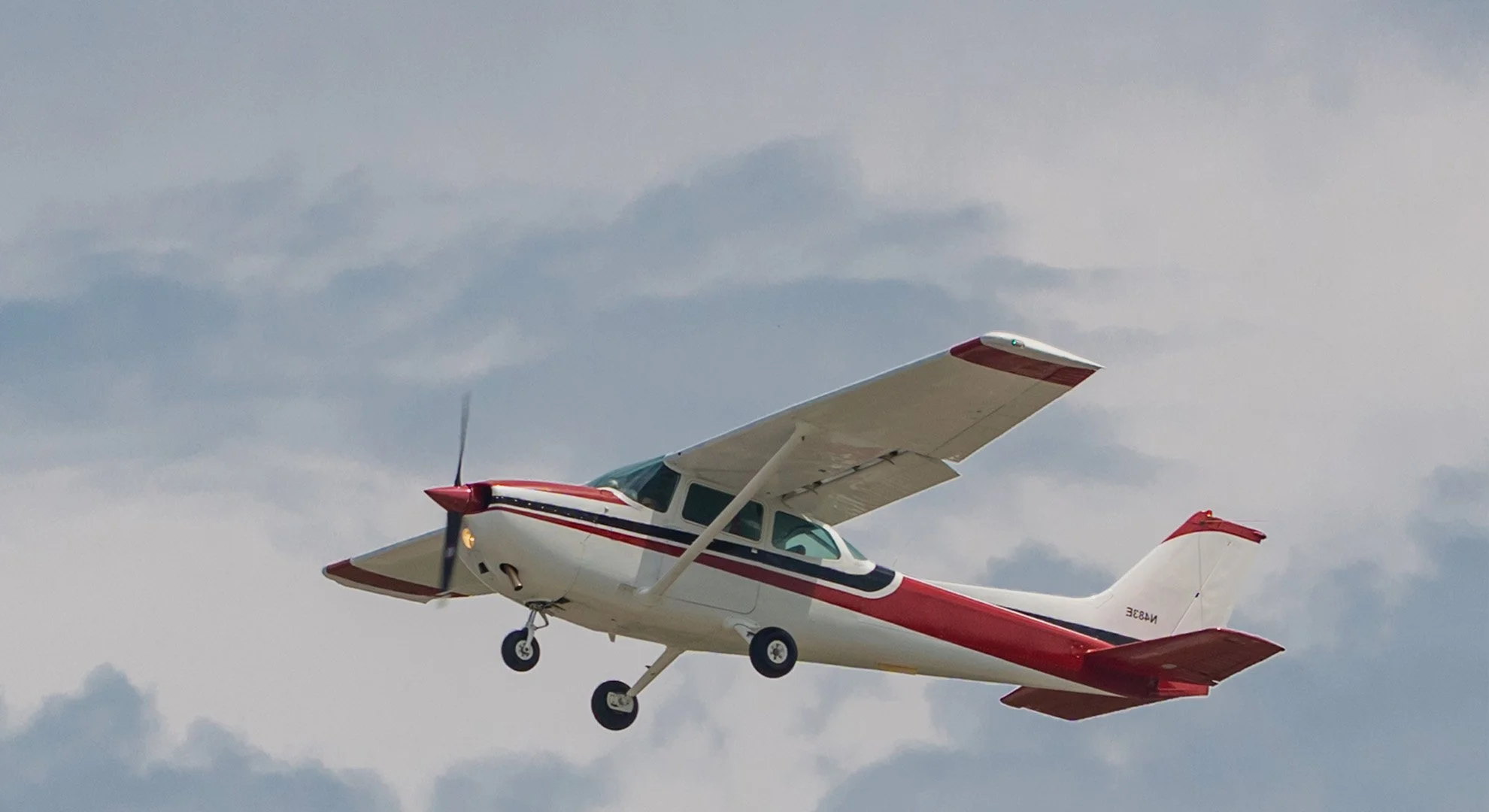 A small white airplane with red and blue stripes flying in the sky with scattered clouds.