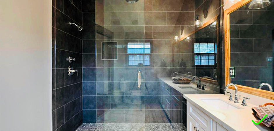 Bathroom with a glass shower enclosure, dark tiled walls, and a white vanity with two sinks and a large mirror.