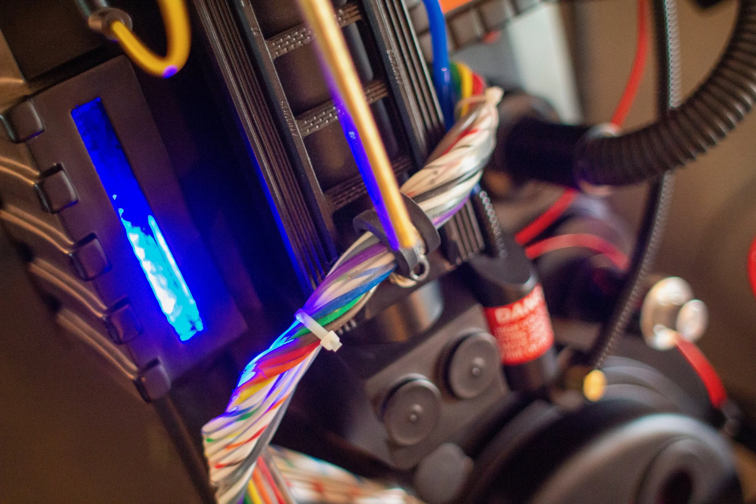 Close-up of a computer hardware component with colorful cables, a blue LED-lit display, and a black device with a red warning label, indicating it is part of a custom-built computer or server setup.