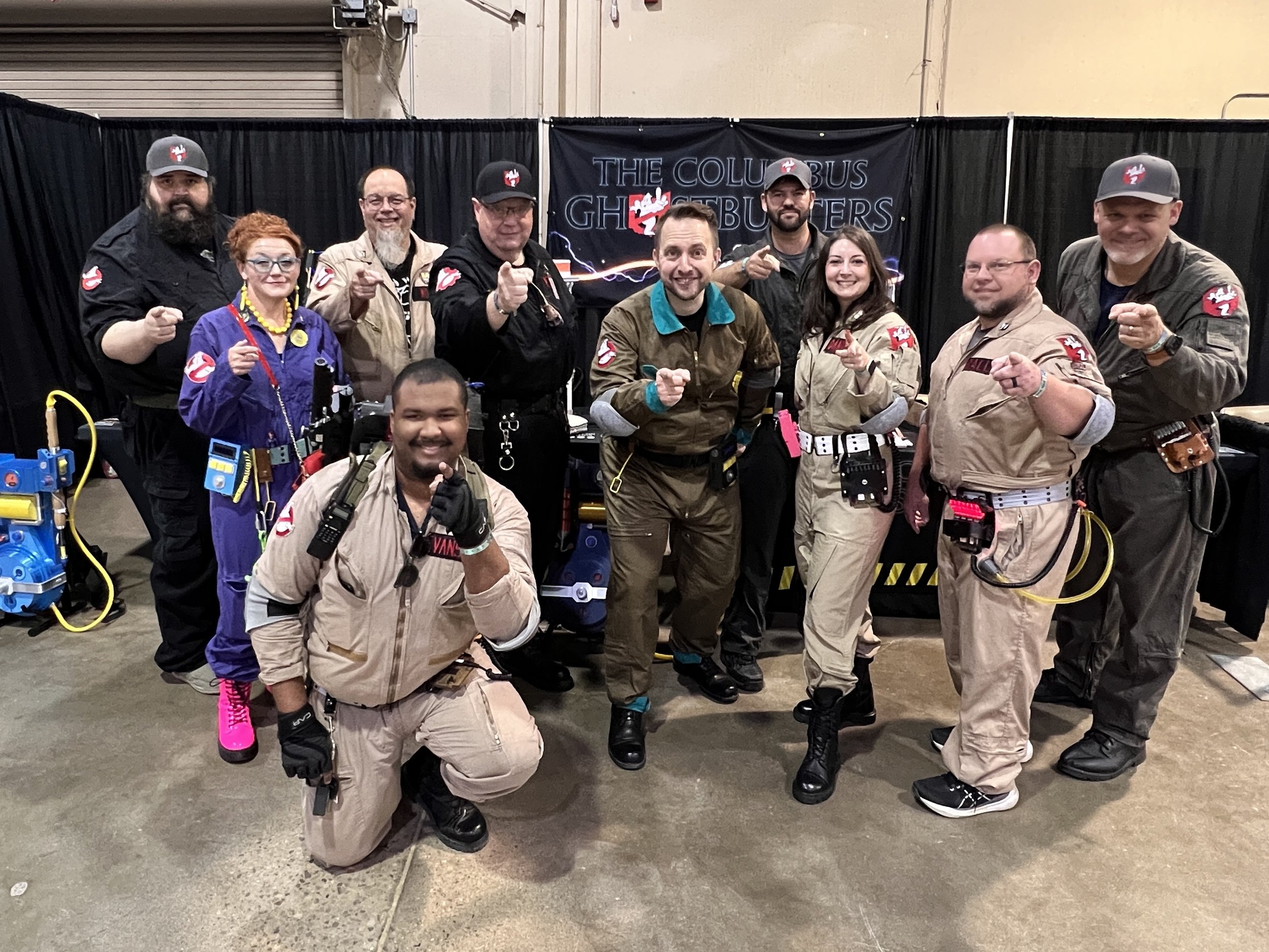 A group of ten people dressed as Ghostbusters characters at a convention or event, standing in front of a black backdrop with "The Columbus Ghostbusters".