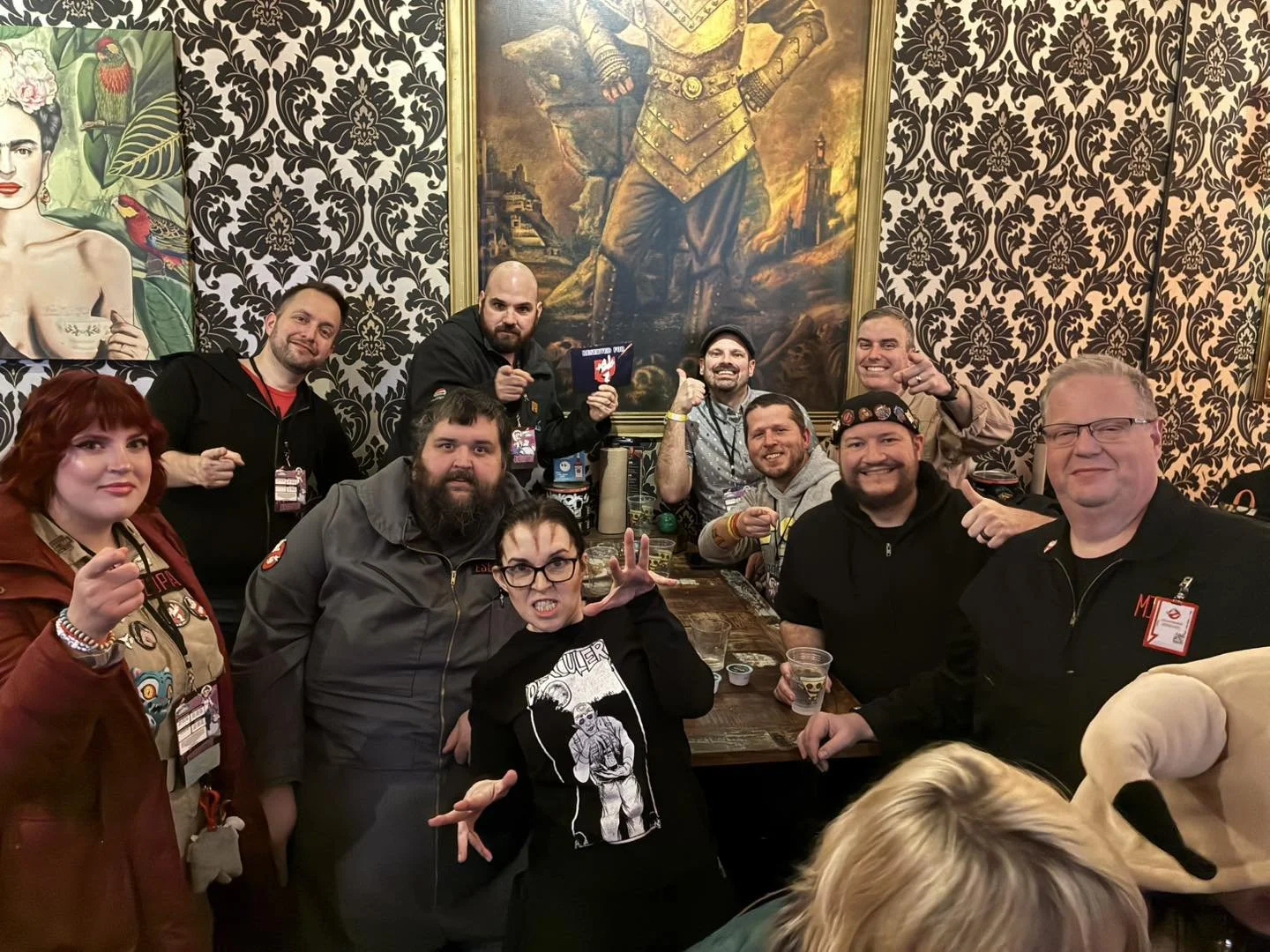 Group of people gathered around a table in a room with ornate wallpaper and large paintings, smiling and posing for the camera.