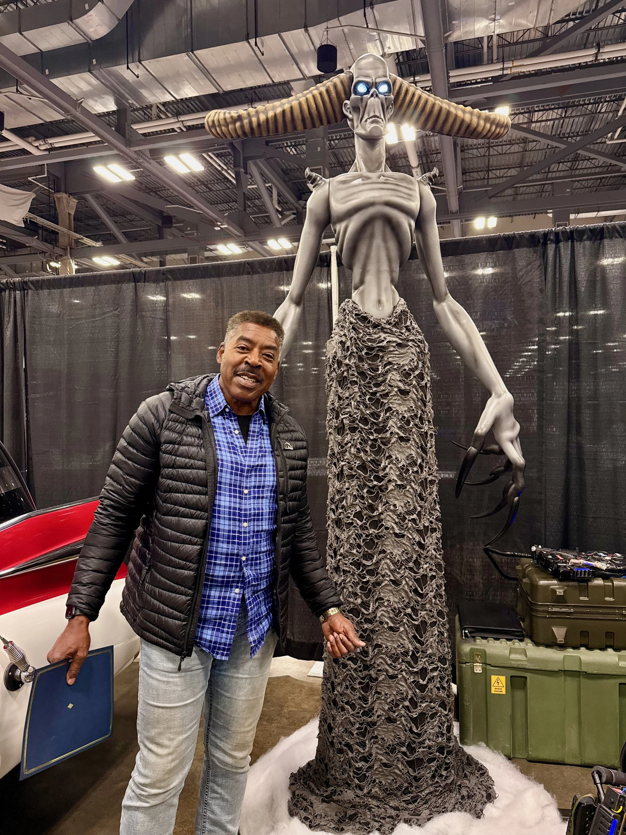 Ernie Hudson standing next to a statue of Garraka in an indoor exhibition space.