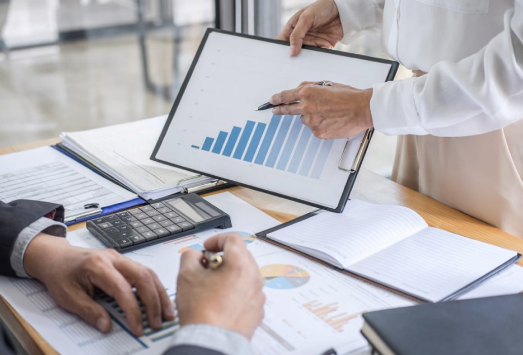 Business professionals analyzing financial charts and data on a tablet, with notebooks, documents, and a calculator on the desk.