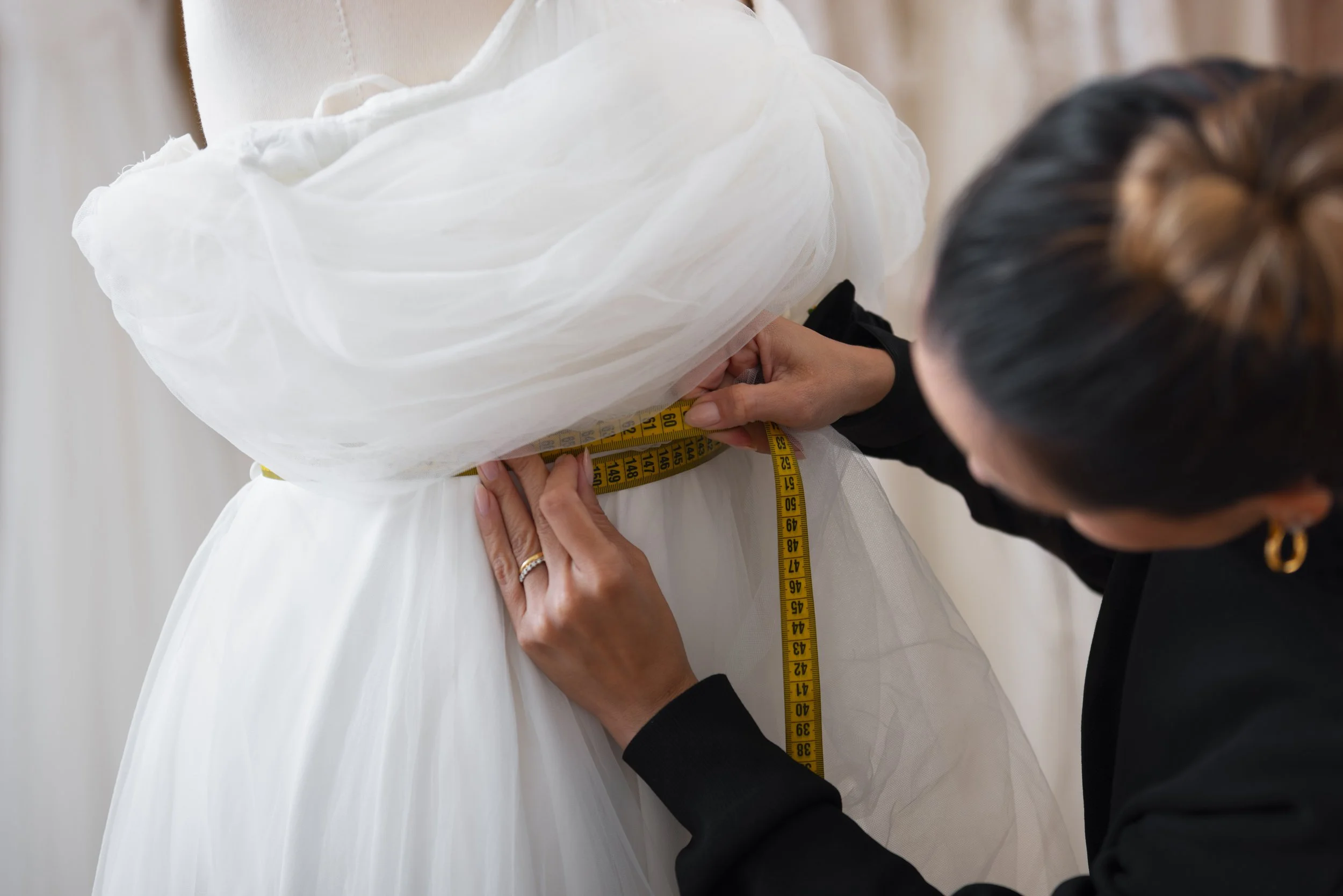 Person measuring the waist of a white dress with a yellow measuring tape.