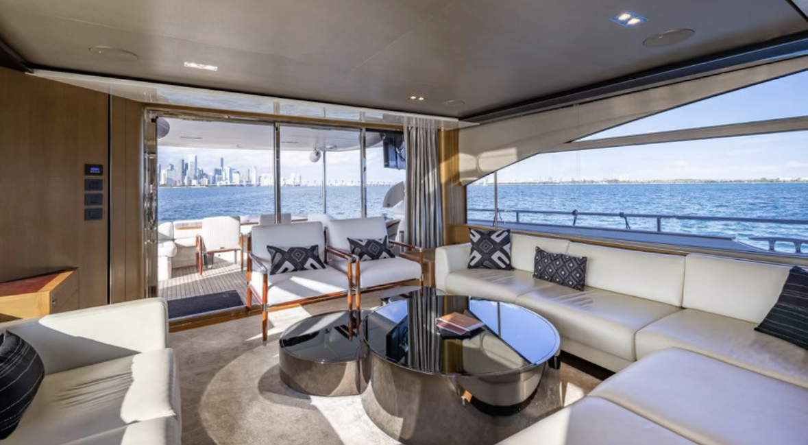 Luxury yacht interior with white leather sofas, black and white patterned cushions, black glossy coffee table, and expansive windows showing water and city skyline.