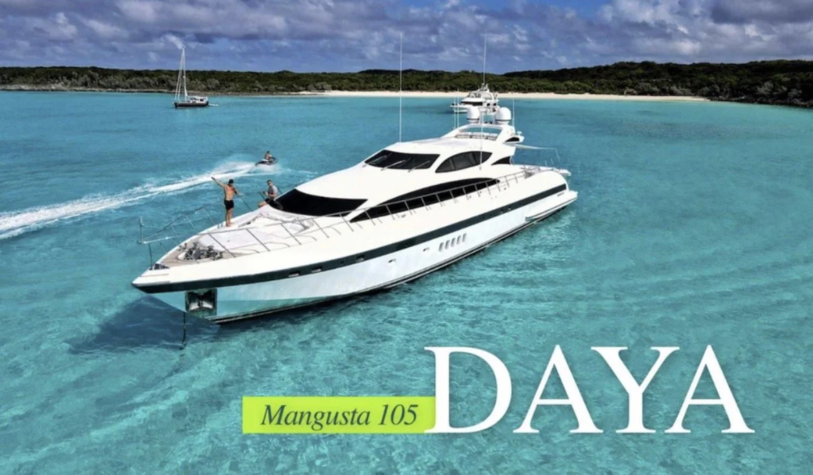A large white yacht with tinted windows anchored in clear blue water near a sandy shoreline with green hills in the background, with people on the yacht and boats nearby, and the words 'Mangusta 105' and 'Daya' overlaid.