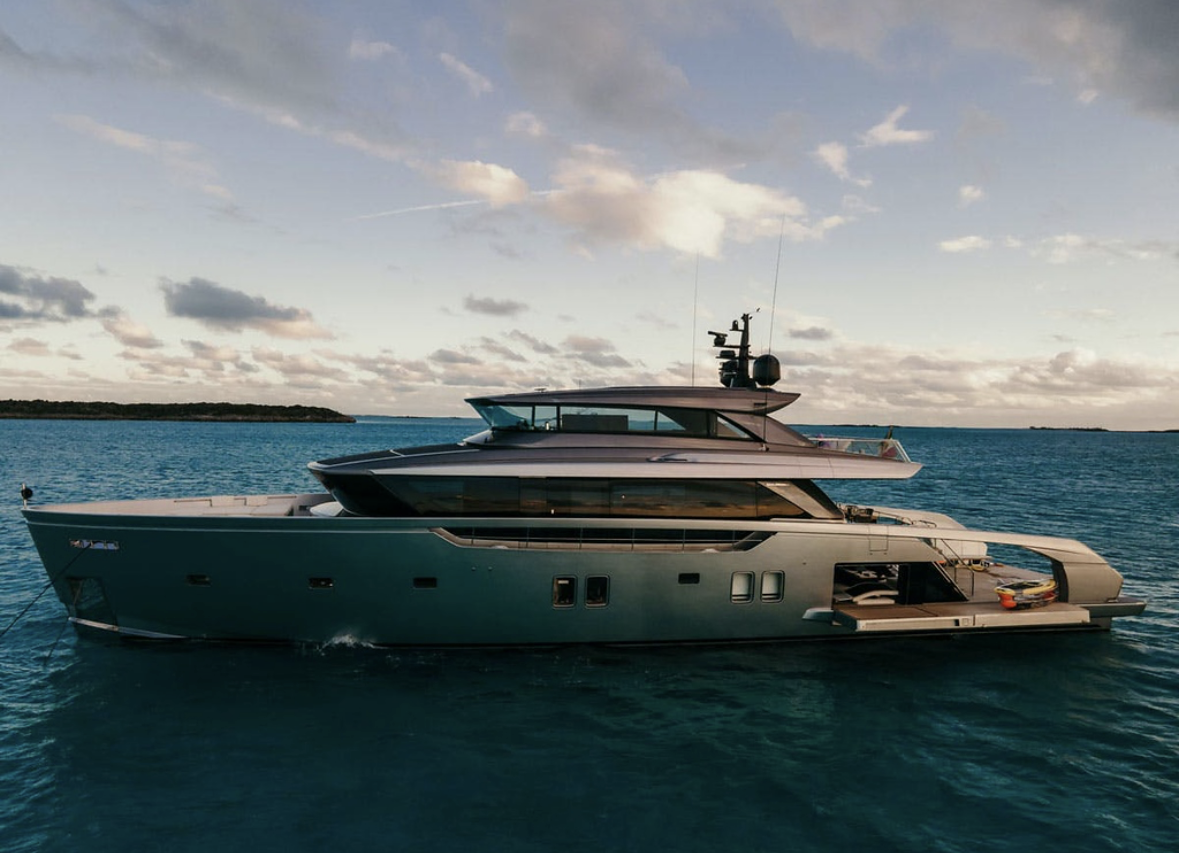 A luxury yacht floating on calm ocean water with a partly cloudy sky overhead and land in the distance.
